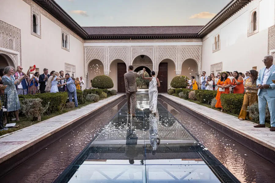 Couple crossing a palace courtyard pool in a shower of petals - luxury wedding photographer Marrakech