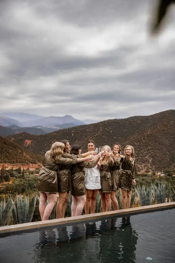 Bridesmaids in olive robes toasting on a terrace above the Atlas Mountains - Atlas Mountains wedding Marrakech
