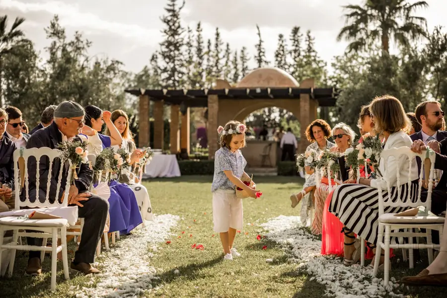 Flower girl walking the petal-strewn garden aisle between seated guests - garden wedding ceremony Marrakech
